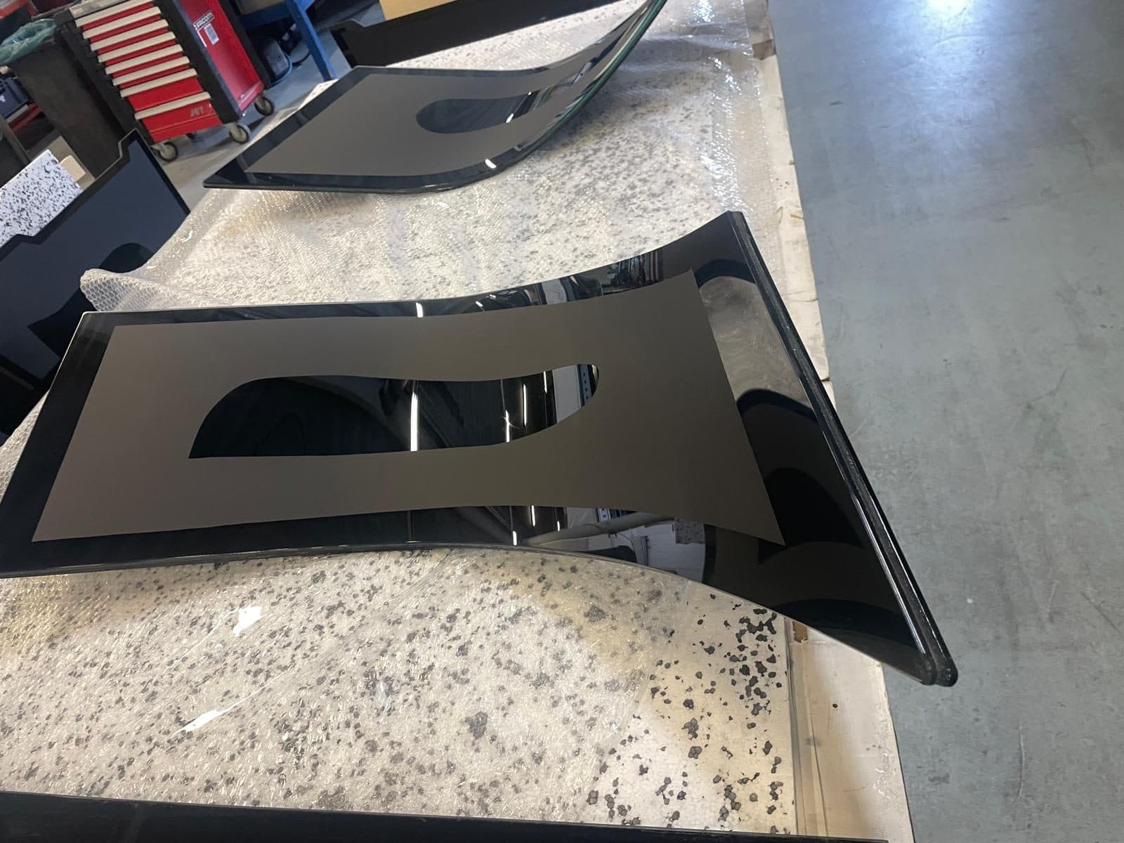 Gebogen glaspanelen met black border folie in de werkplaats, klaar om op maat gesneden te worden